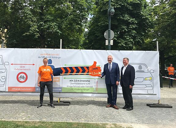 Eva Mahling vom ADFC München zeigt den Ministern Herrmann und Bernreiter den erforderlichen Abstand beim Überholen von Radfahrenden