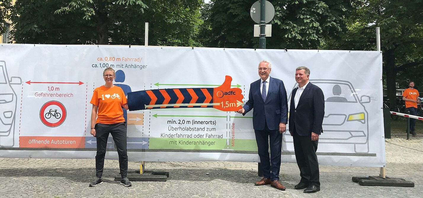 Eva Mahling vom ADFC München zeigt den Ministern Herrmann und Bernreiter den erforderlichen Abstand beim Überholen von Radfahrenden