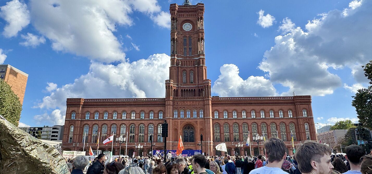 Ein Menschenmenge mit Fahnen und Transparenten vor dem Roten Rathaus Berlin ist zu sehen. 