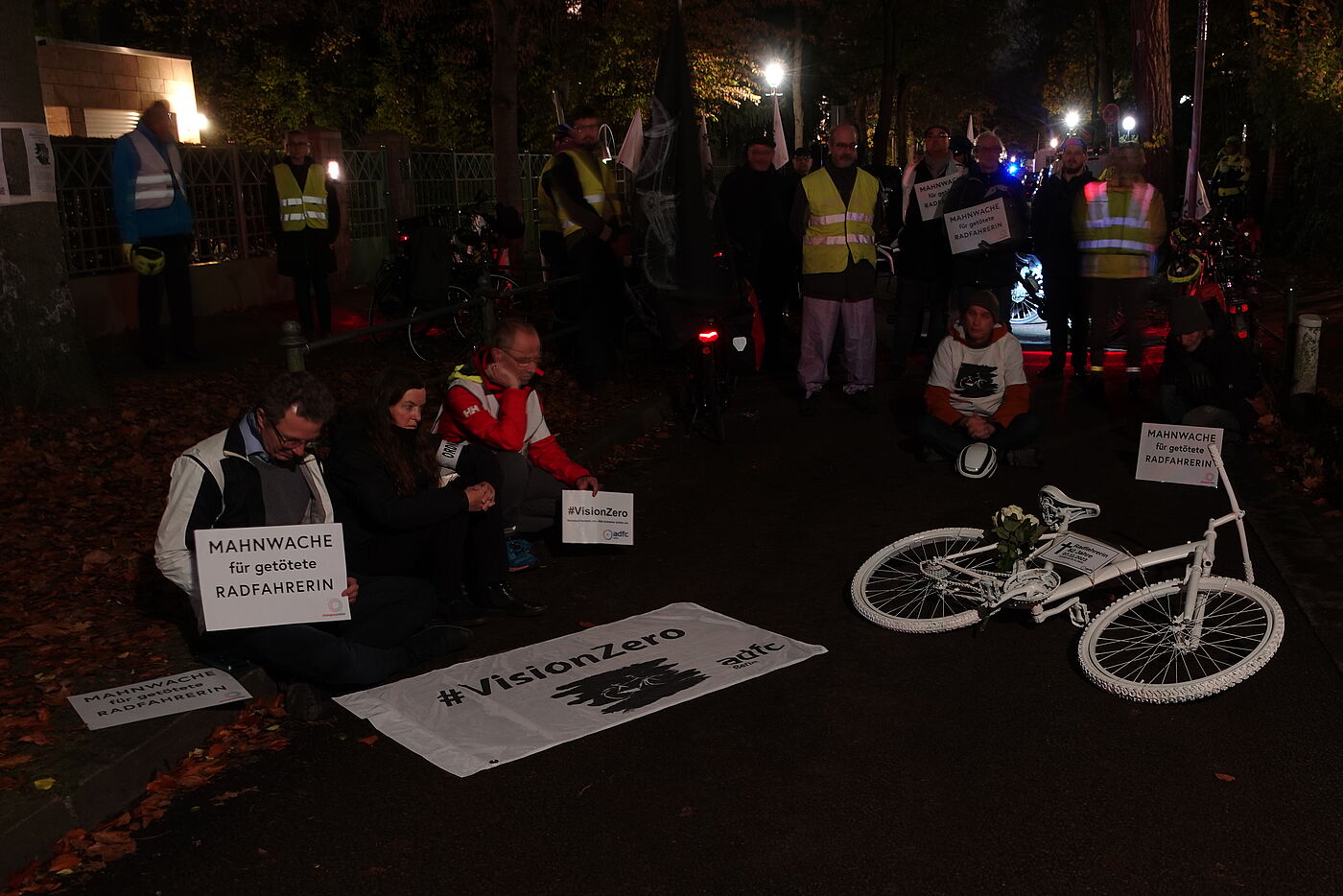 Geisterrad 9-11-2023 Mahnwache Menschen sitzen bei einer Mahnwache um ein weißes Geisterrad auf der Straße