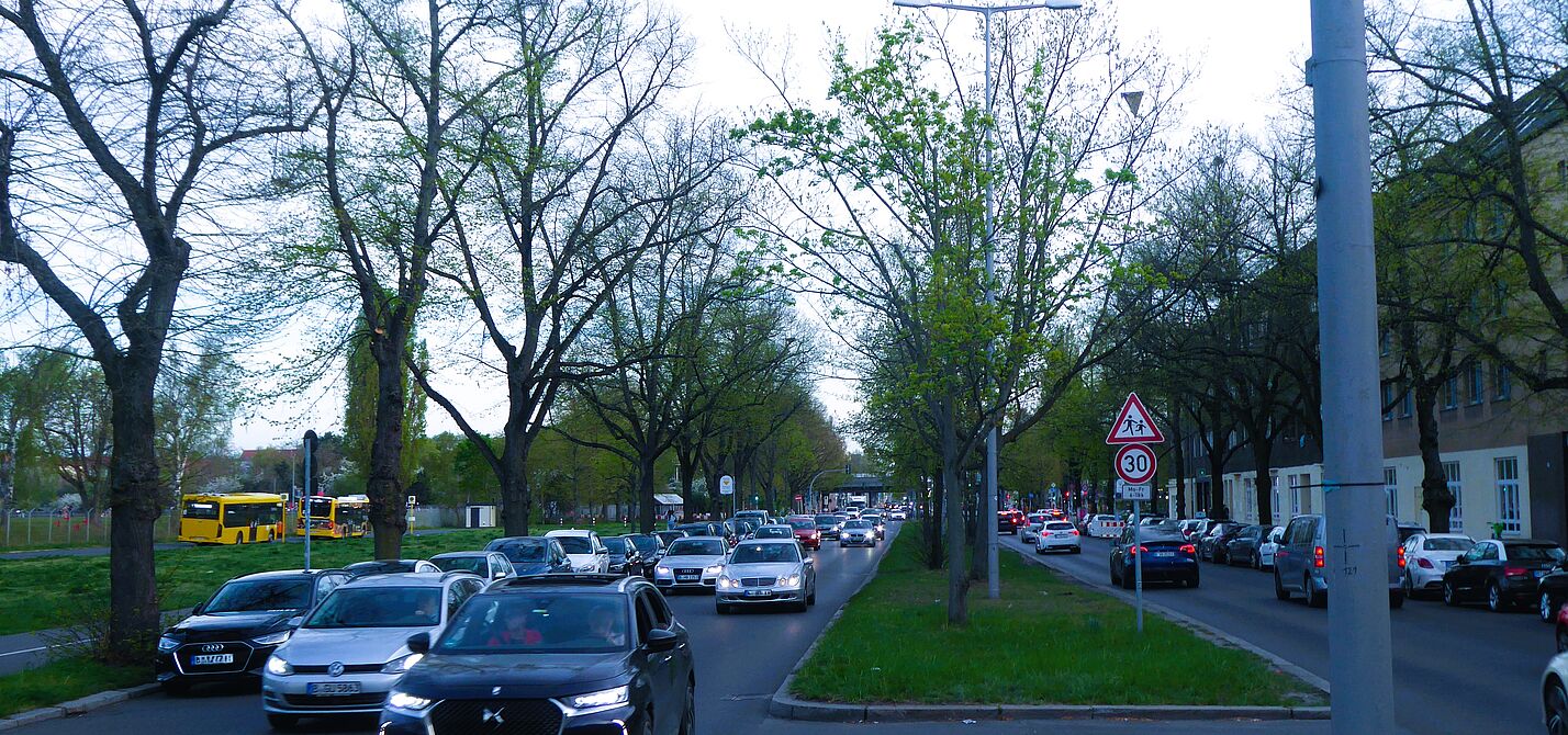 Foto vom Tempelhofer Damm, vom begrünten Mittelstreifen aus Richtung Süden betrachtet. Rechts und links fahren auf jeweils zwei Fahrspuren Autos. Sowohl auf dem Mitteistreifen als auch am Fahrbahnrand stehen Bäume.