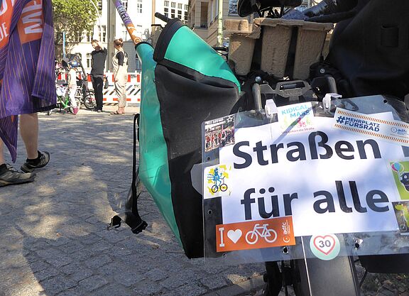 Auf einem Schild, das am Gespäckträger eines Fahrrads hängt, steht "Straßen für alle".