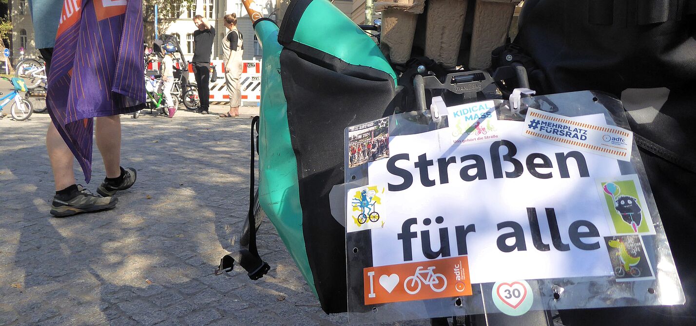 Auf einem Schild, das am Gespäckträger eines Fahrrads hängt, steht "Straßen für alle".