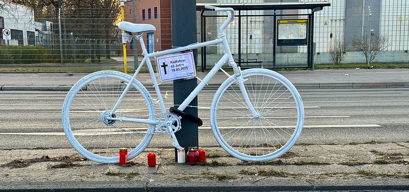 Geisterrad Neukölln 2025 ein weißes Geisterrad mit Informationsschild "Radfahrer 63 Jahre" und Vision Zero Fahne im Vordergrund