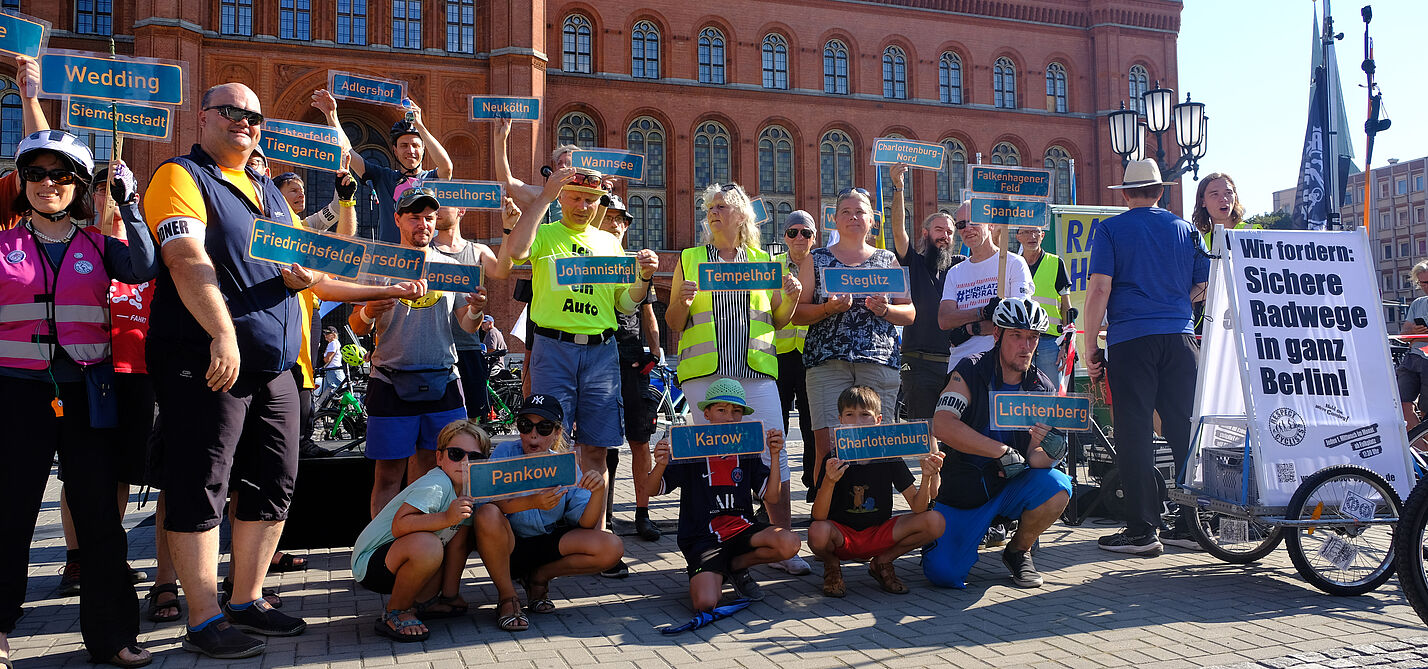 Menschen halten vor dem Roten Rathaus diverse Berliner Ortsteilschilder in die Höhe