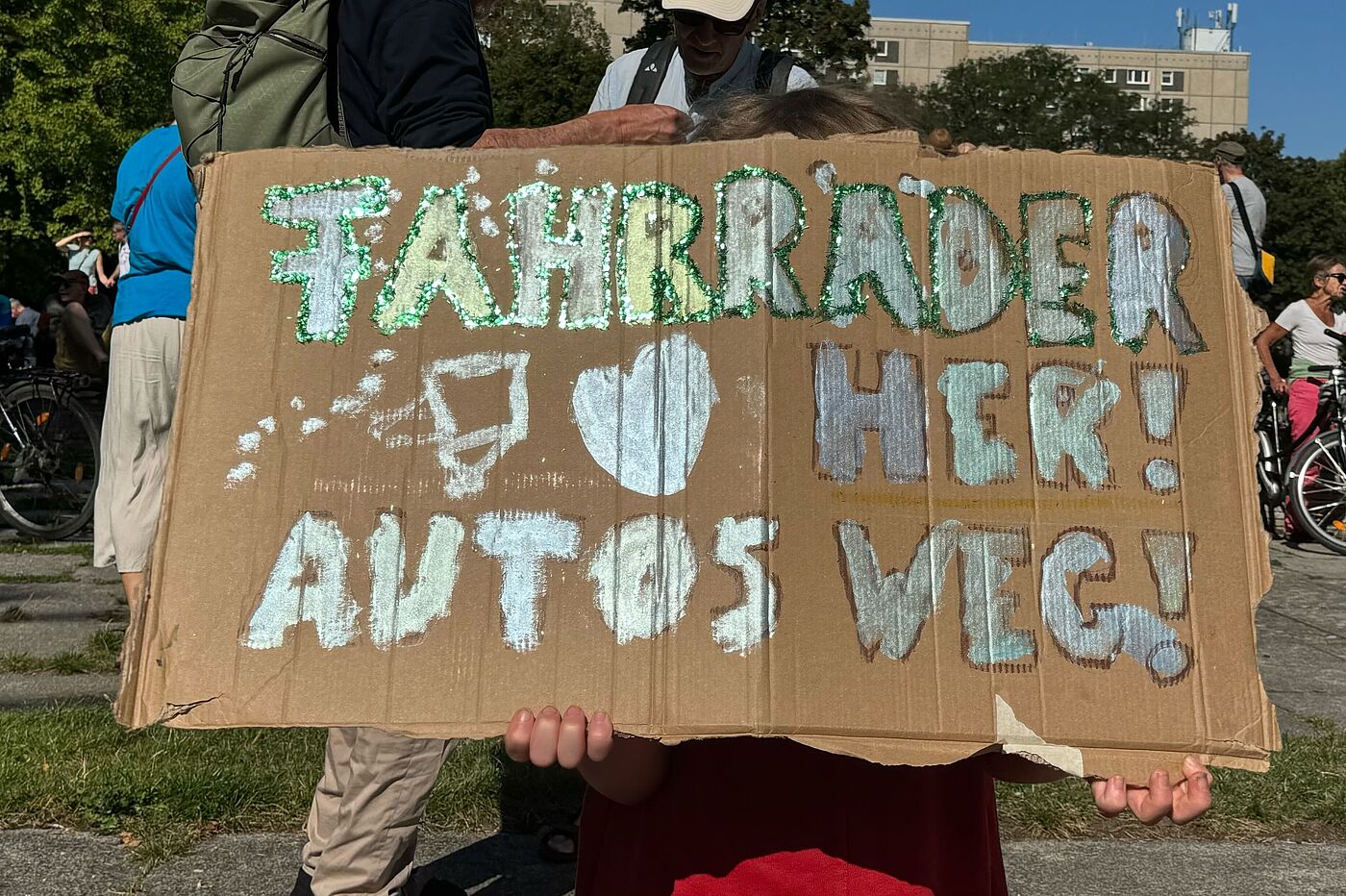 Ein Kind hält ein Schild hoch auf dem steht: Fahrräder her, Autos weg!