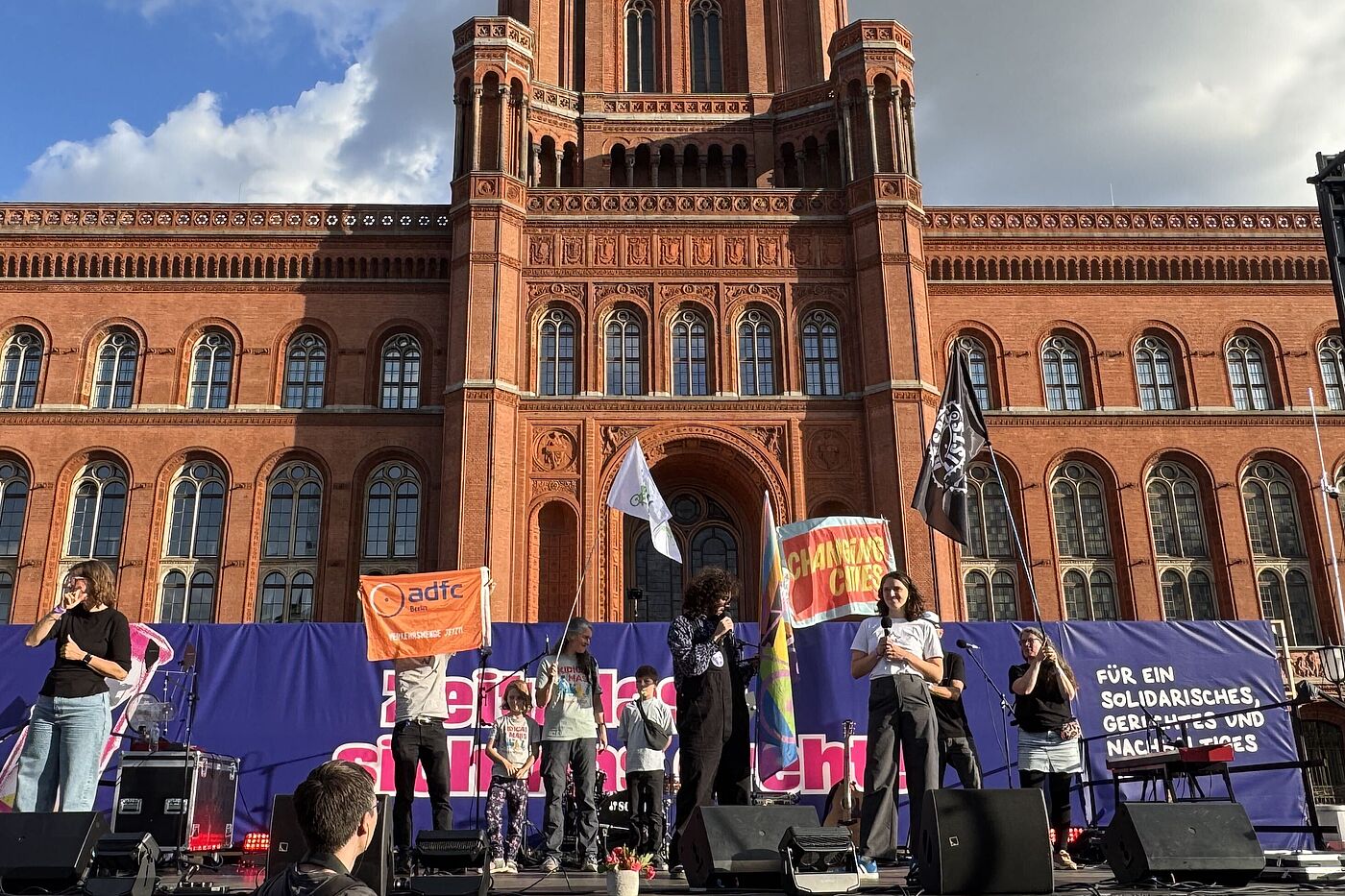 Im Hintergrund ist das Rote Rathaus, davor eine Bühne, auf der zwei Personen sprechen und Fahnen von Changing Cities und ADFC Berlin zu sehen sind. 
