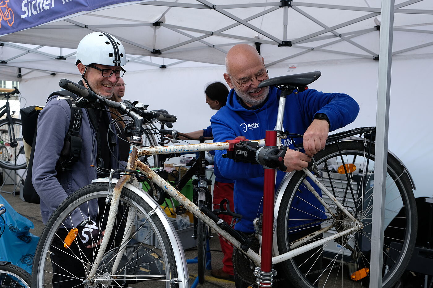 Fahrrad-Check Velo 2023 Fahrrad-Mechaniker repariert das Fahrrad eines Manns der mit Helm daneben steht