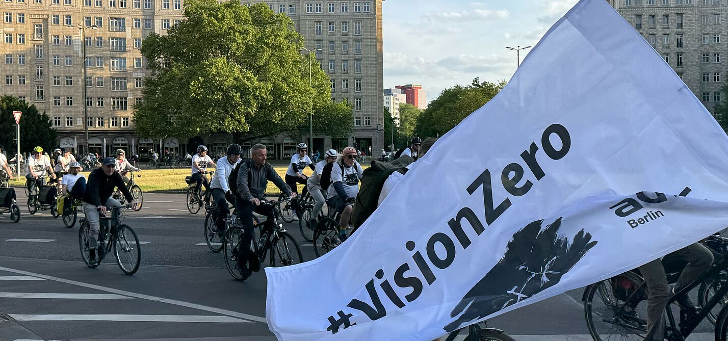 weiße Vision Zero Fahne weht vor Radfahrenden 