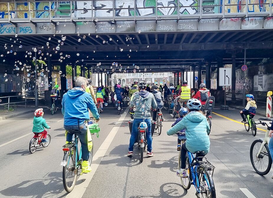 Kidical Mass Schöneberg am 17. Mai 2025 auf der Yorckstraße Richtung Treptow-Köpenick: Wir fordern sichere Straßen für alle! Auf dem Foto ist eine Gruppe Radfahrender mit Kindern unter den Yorckbrücken zu sehen, sie sind von hinten aufgenommen. Die bunte Kleidung wird durch aufsteigende Seifenblasen unterstrichen.