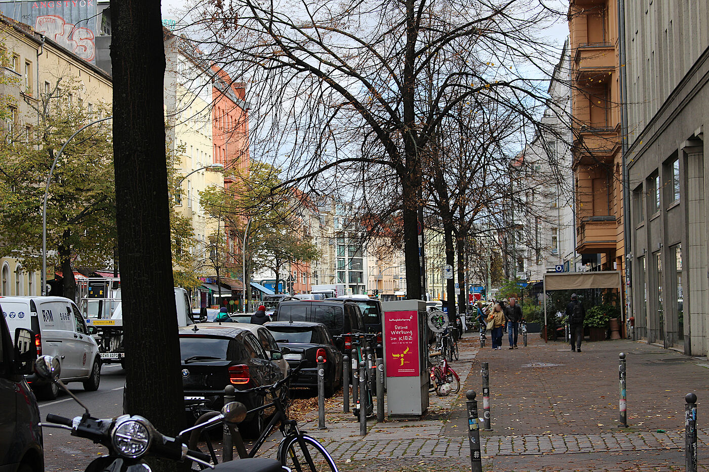 Gehweg vor Rosenthaler Platz Ansicht der Torstraße vom Gehweg aus, links Bäume, rechts Vorbauten von Gastronomie, dazwischen gerade mal Platz für 2 Fußgänger:innen