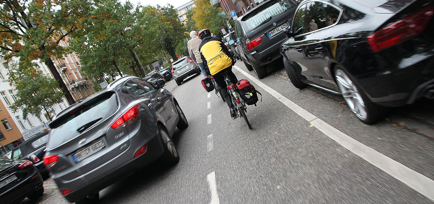 Radfahrende auf schmalem Schutzstreifen werden zu eng überholt Radfahrender fährt neben parkenden Autos und wir von fahrenden Kfz zu knapp überholt.