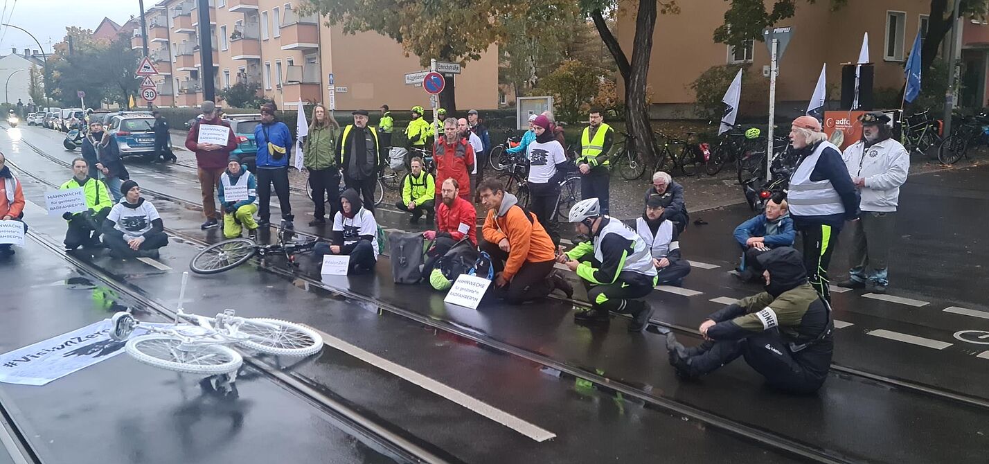 Mahnwache 23-10-27 Menschen sitzen bei einer Mahnwache auf der Straße um ein weißes Geisterrad