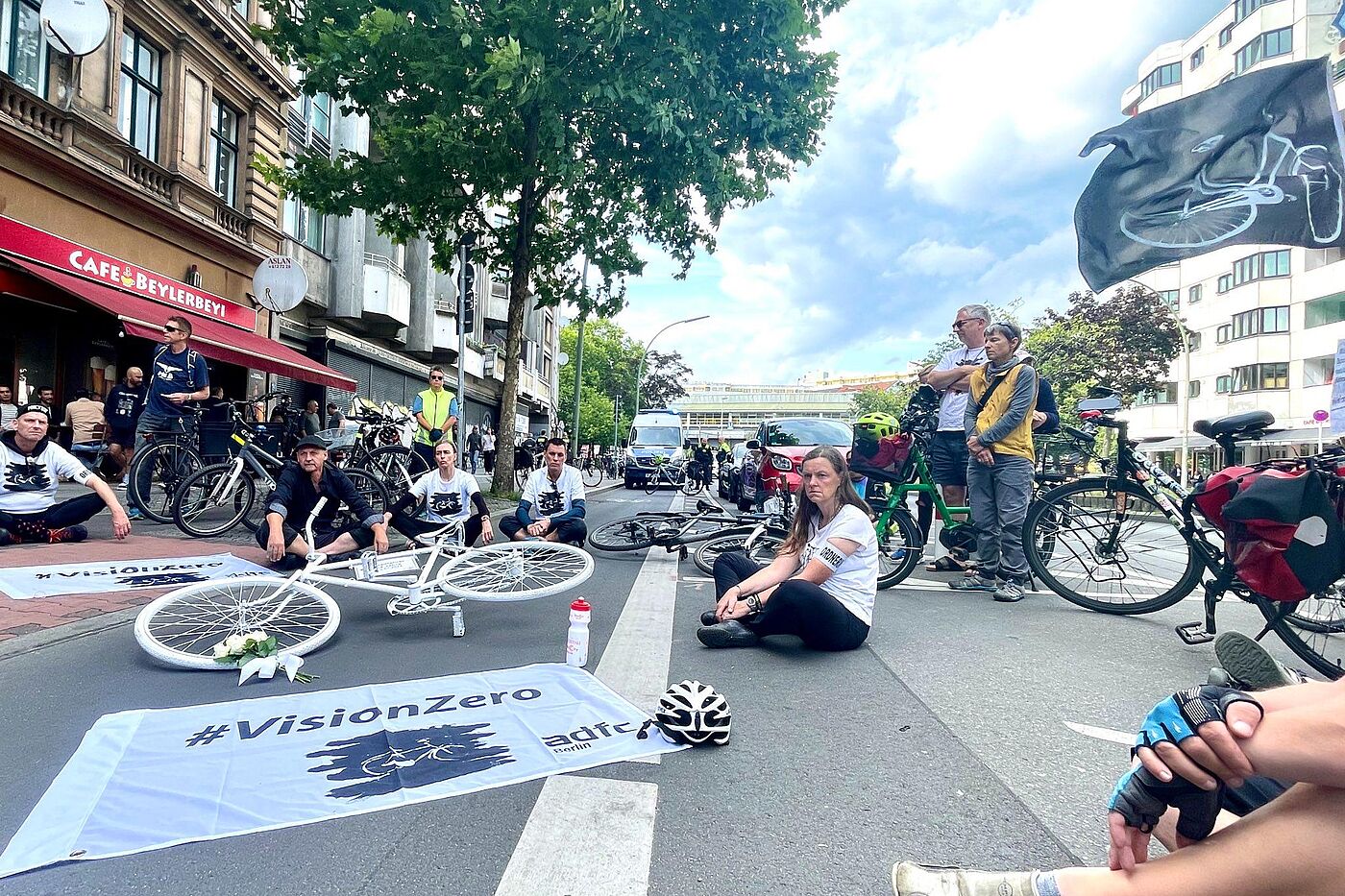 Mahnwache am 22. Juli 2023 für den verstorbenen Radfahrer in Kreuzberg Menschen sitzen um ein weißes Geisterrad und eine Fahne mit Vision Zero