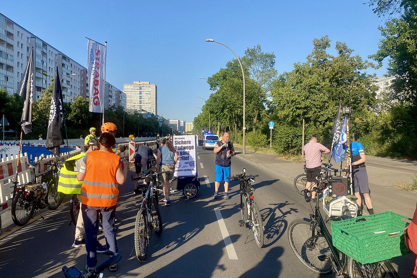 Ansprache auf der Landsberger Allee in Lichtenberg bei einer Respect Cyclists Demo Eine Gruppe Radfahrender steht mit Fahnen auf der Landsberger Allee und hört einem Sprecher zu, der eine Zwischenkundgebung hält.