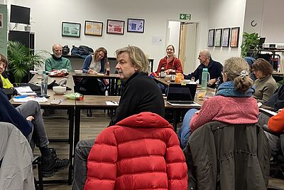 ADFC Schöneberg bei einem Treffen im Raum für Beteiligung Eine Gruppe Menschen sitzt in einem großen, hell erleuchteten Raum um Tische, die im Kreis aufgestellt sind.