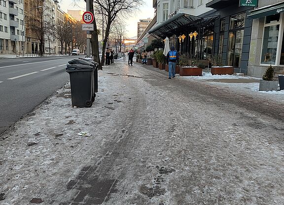 Im rechten Bereich ist ein vereister Gehweg und nicht erkennbar Radweg zu sehen, links davon ist Schnee- und Eis-freier Asphalt auf der Fahrbahn
