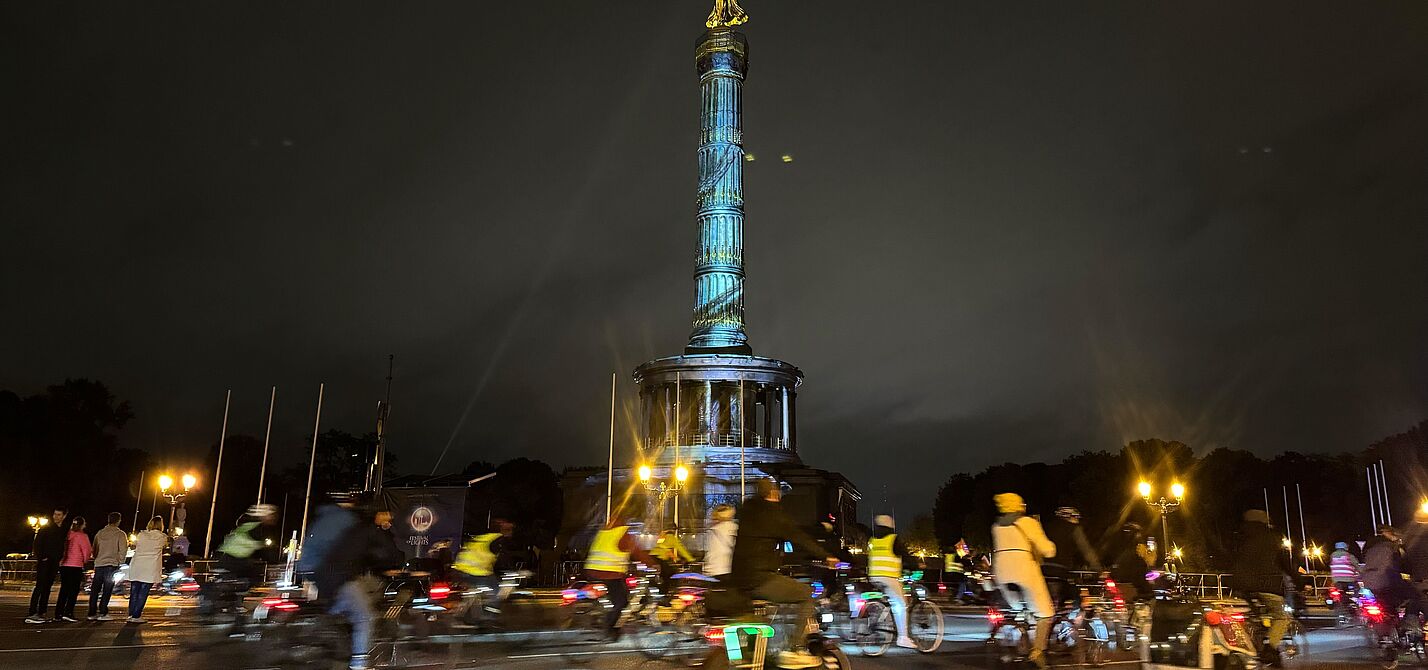 Siegessäule in Berlin wird angestrahlt, leuchtende Radfahrende herum