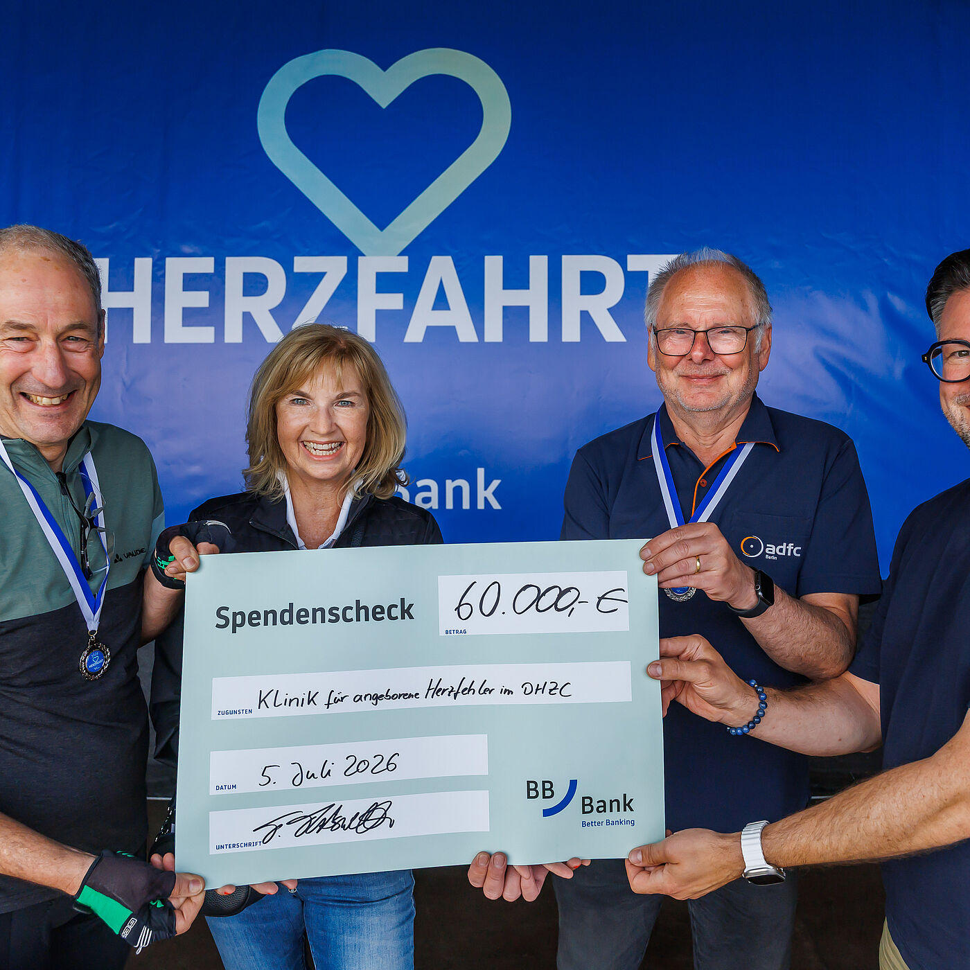 HerzFahrt 2026 Spendencheck Vier Menschen halten einen Spendencheck über 60.000€ bei der HerzFahrt