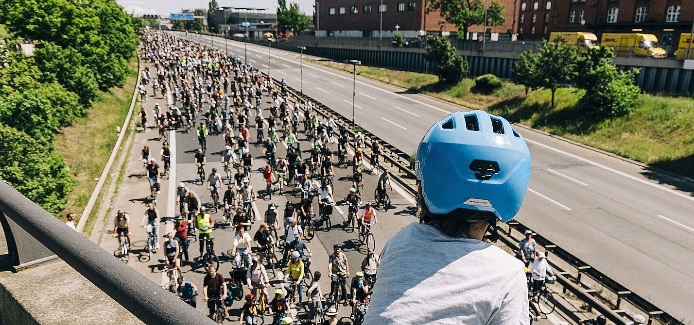 ADFC-Sternfahrt Kind mit blauem Helm guckt auf Autobahn über die auf einer Seite hunderte FahrradfahrerInnen fahren
