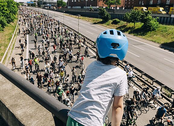 ADFC-Sternfahrt Kind mit blauem Helm guckt auf Autobahn über die auf einer Seite hunderte FahrradfahrerInnen fahren