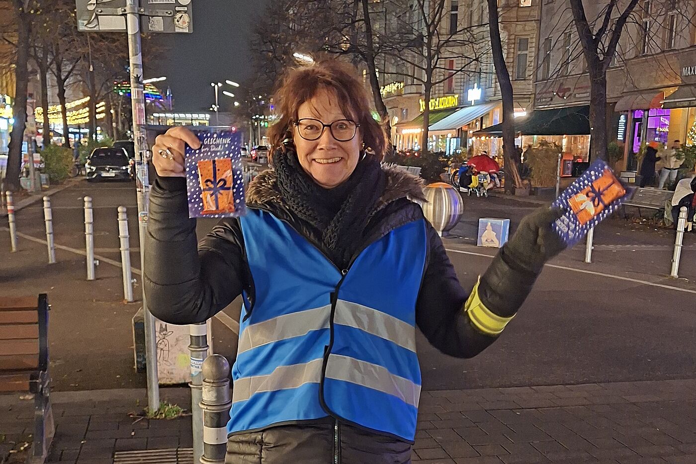 ADFC Lebkuchen-Aktion am Winterfeldtplatz in Berlin Schöneberg Eine Frau mit blauer Warnweste steht auf dem Winterfeldtmarkt in Berlin Schöneberg. Sie hält zwei Karten des ADFC mit einem Lebkuchen in Händen.