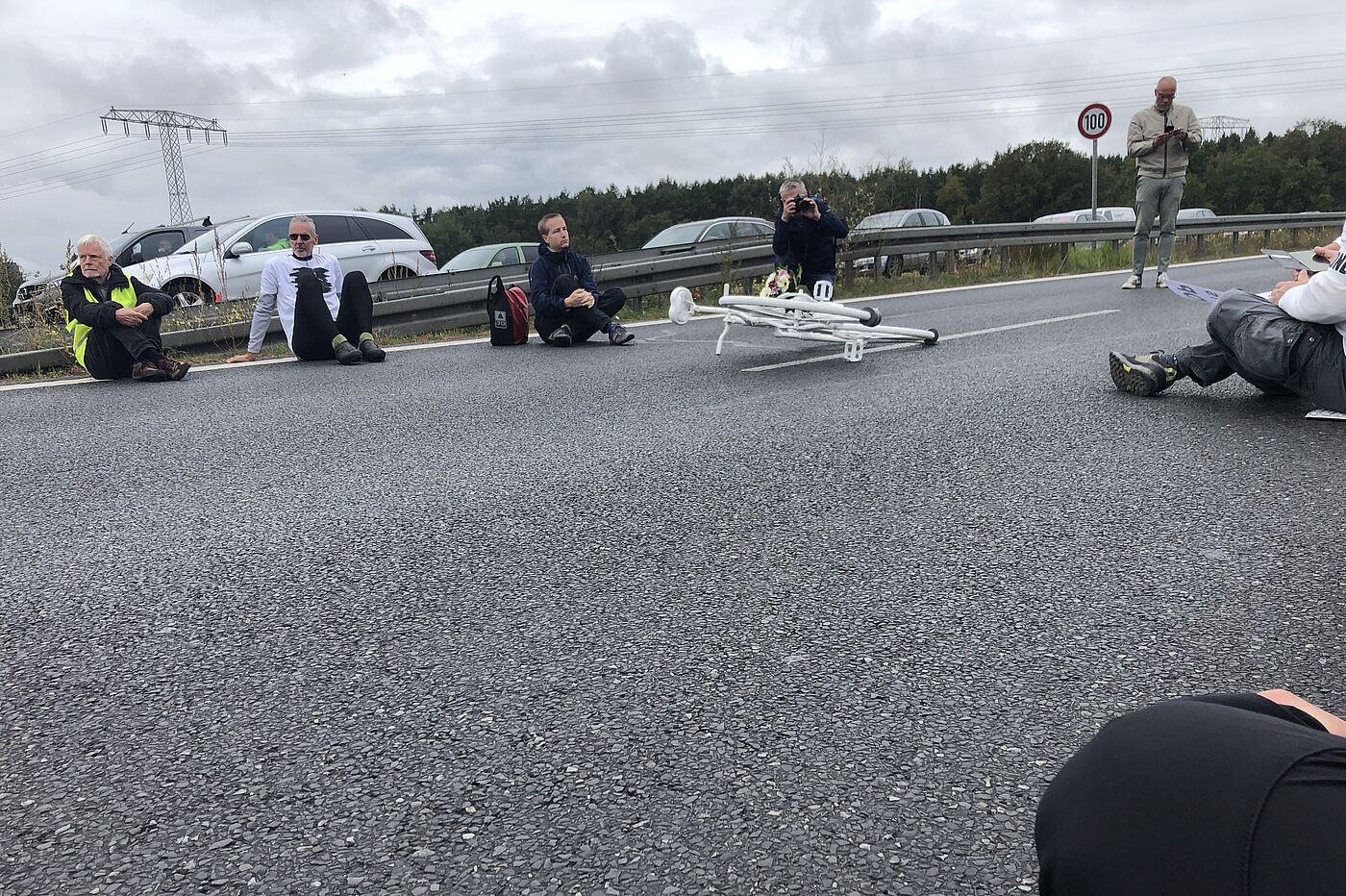 Menschen sitzen bei einer Mahnwache um ein weißes Fahrrad auf der Straße