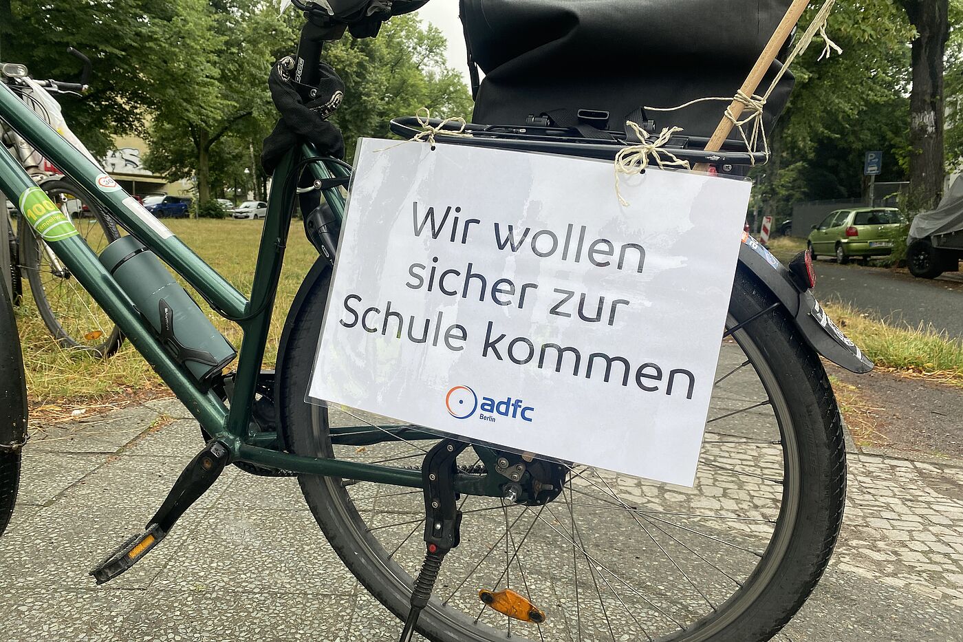 Für geschützte Radwege und sichere Schulwege auf der Marienfelder Allee! Laminiertes Schild des ADFC Berlin mit der Aufschrift "Wir wollen sicher zur Schule kommen!"